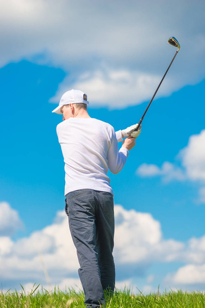 man swinging his club before hitting the ball against the blue s - Foto, imagen