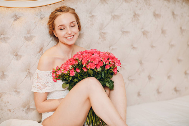 Όμορφη νεαρή γυναίκα στην κρεβατοκάμαρα και λουλούδια - Φωτογραφία, εικόνα