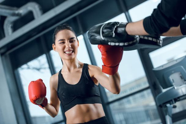 expressivo jovem boxeador do sexo feminino exercitando com treinador no ginásio
 - Foto, Imagem
