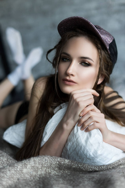 Portrait of a beautiful girl wearing a baseball cap on the bed - Fotoğraf, Görsel