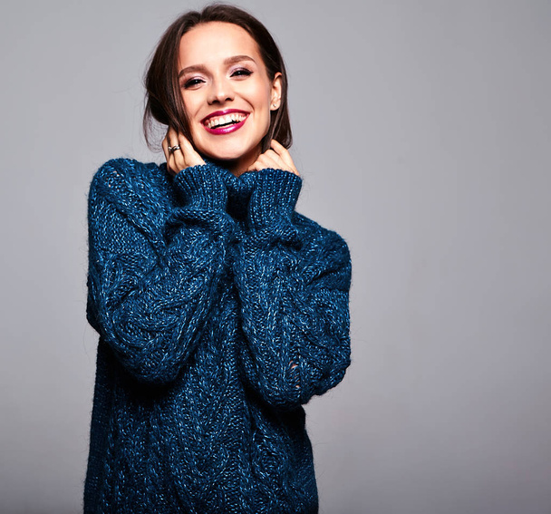 Portrait of beautiful smiling cute brunette woman model in casual blue sweater clothes with bright makeup and red lips isolated on gray - Φωτογραφία, εικόνα