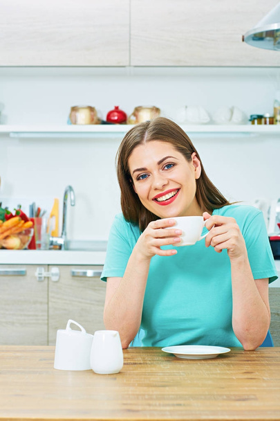 Smiling beautiful casual dressed woman drinking coffee in kitchen at home - Valokuva, kuva