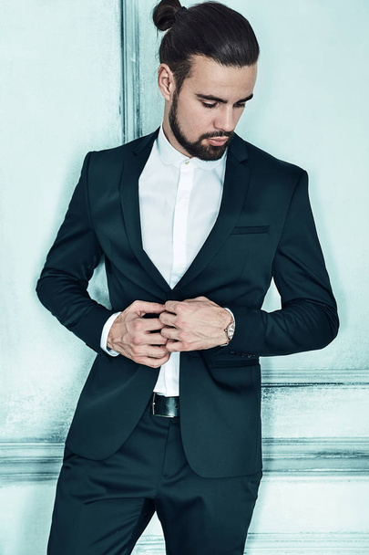 portrait of handsome fashion stylish hipster lumbersexual businessman model dressed in elegant black suit in posing near light blue wall in studio. Metrosexual - Foto, afbeelding