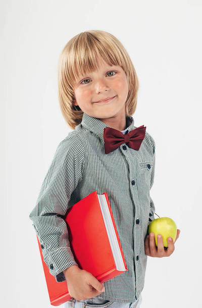Muotokuva onnellinen koulupoika pukeutunut punainen rusetti omena ja punainen kirja eristetty valkoisella pohjalla. Esikoulu
.  - Valokuva, kuva