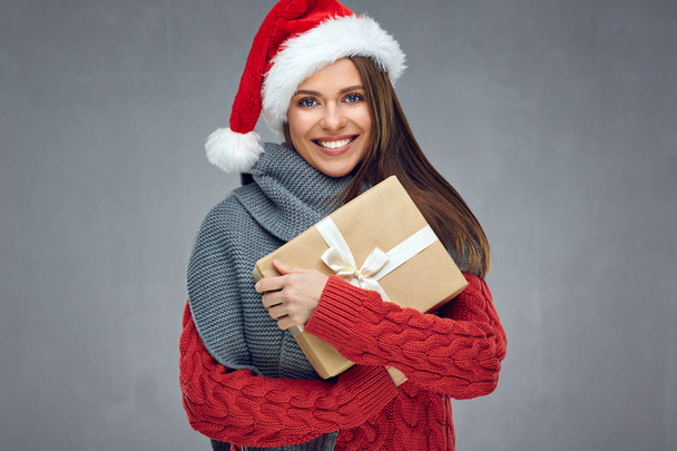 happy woman wearing knitted sweater and Santa hat holding Christmas gift   - Zdjęcie, obraz