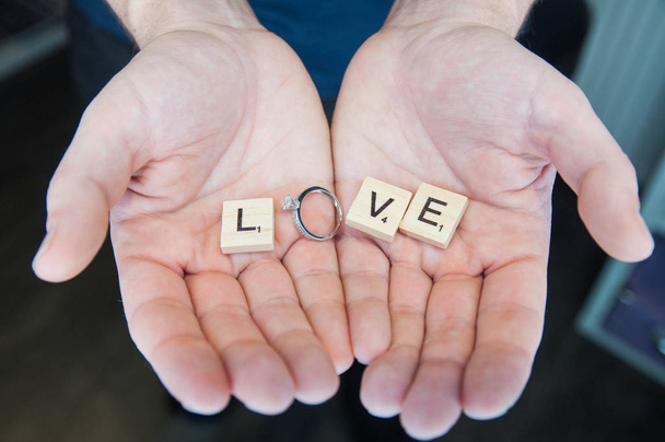 Ξύλινο γράμμα της αλφαβήτου μπλοκ κεραμίδια έννοια αγάπης για την ημέρα του Αγίου Βαλεντίνου με το γαμήλιο δαχτυλίδι στα χέρια του ο άνθρωπος - Φωτογραφία, εικόνα