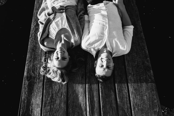 Zwart-wit beeld van een mooie jonge paar ligt op een houten achtergrond, kijkt naar de camera en lachend. Bovenaanzicht. Liefdesverhaal - Foto, afbeelding