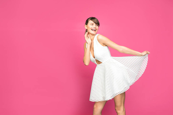 young and pretty woman posing and smiling in white summer dress on pink background - Foto, immagini