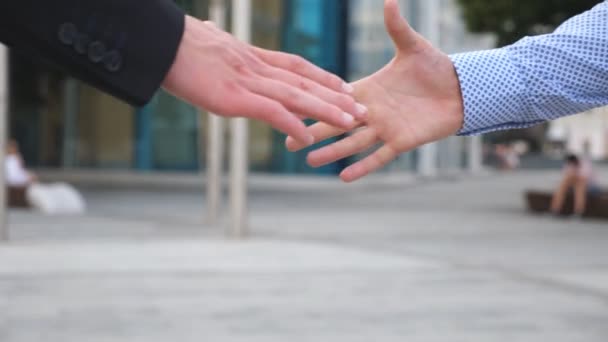 Colleagues meet and shake hands in the city background. Two businessmen greeting each other in urban environment. Business handshake outdoor. Shaking of male arms outside. Close up Slow motion - Footage, Video