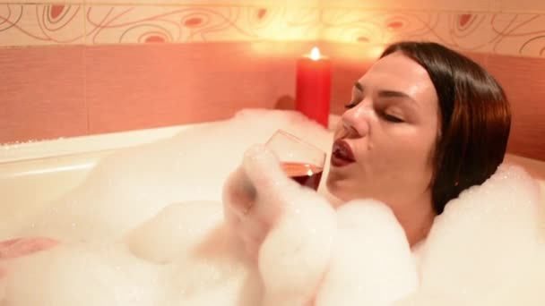 Hermosa chica tomando un baño de burbujas con una copa de vino. Un gran baño blanco y alegría en su cara. concepto de relajación
 - Imágenes, Vídeo