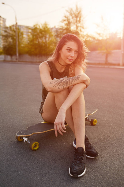 Nuori tyttö lyhyissä shortseissa istuu longboard
 - Valokuva, kuva