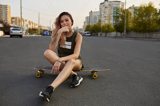 junges Mädchen in kurzen Shorts auf Longboard sitzend - Foto, Bild