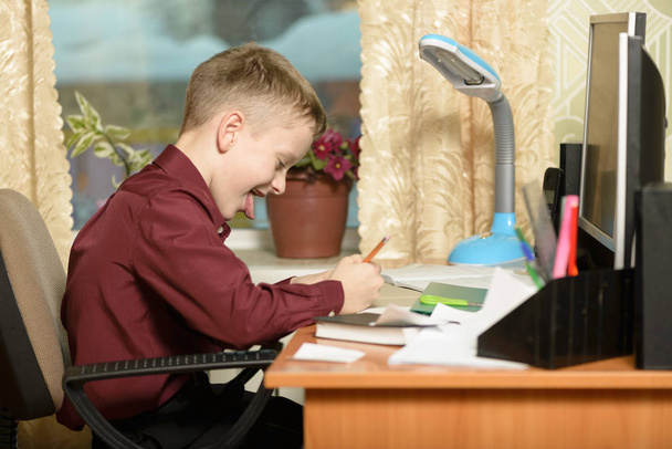 der Kerl im Büro benutzt Computertechnologie. Er schreibt seine Gedanken auf ein Blatt Papier. sitzt in einem Sessel in einem weinroten Hemd. Er streckt seine Zunge aus. - Foto, Bild