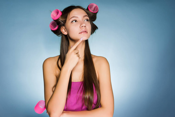 pensive woman with curlers on head on blue background - Foto, afbeelding