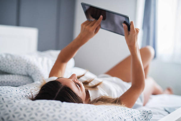 красива жінка лежить на ліжку і використовує планшетний ПК вдома
 - Фото, зображення