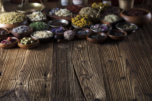 Alternative medicine. Herbs in bowls, mortar and medicine bottles on wooden rustic table. - Photo, Image