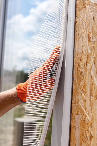 Bauarbeiter tragen Handschuhe und installieren ein spezielles Gitter am Fenster. Bauarbeiten. - Foto, Bild