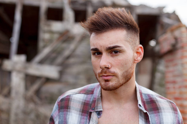 atrakcyjny facet ubrany plaid shirt rozpiętym przeciwko opuszczony dom - Zdjęcie, obraz