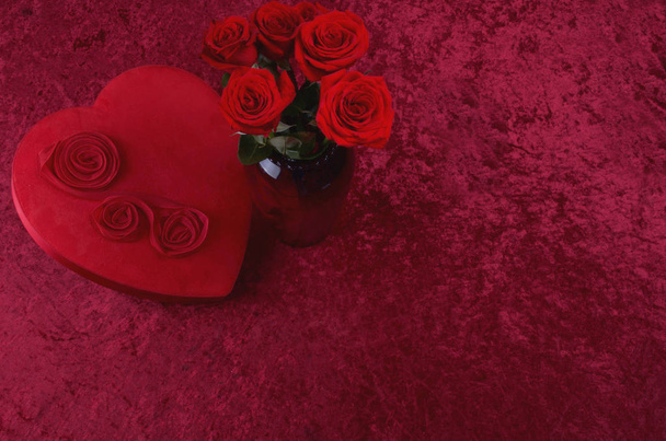 Cena dos namorados com caixa de chocolate em forma de coração, um monte de rosas em fundo de veludo esmagado vermelho e corredor de renda branca
 - Foto, Imagem