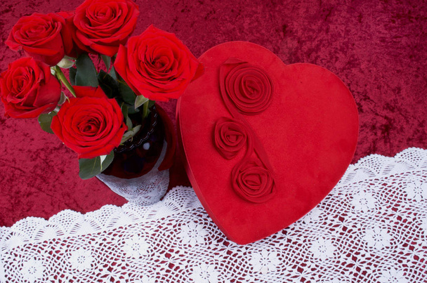 Cena dos namorados com caixa de chocolate em forma de coração, um monte de rosas em fundo de veludo esmagado vermelho e corredor de renda branca
 - Foto, Imagem