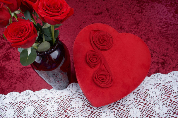 Valentinsszene mit herzförmiger Schokoladenschachtel, Rosenstrauß auf rotem, zerkleinertem Samthintergrund und weißem Spitzenläufer - Foto, Bild