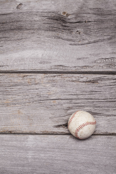Een versleten honkbal zit op een rustieke houten achtergrond. De foto werd geschoten in portret formaat maar kan worden gedraaid in landschap. - Foto, afbeelding