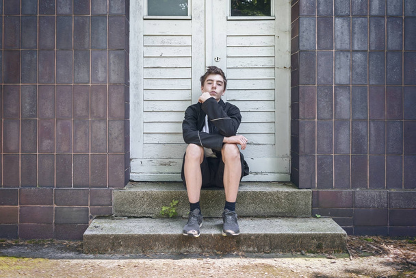 Egy ajtó előtt ülve, a lépcsőn egy fiatalember portréja - Fotó, kép