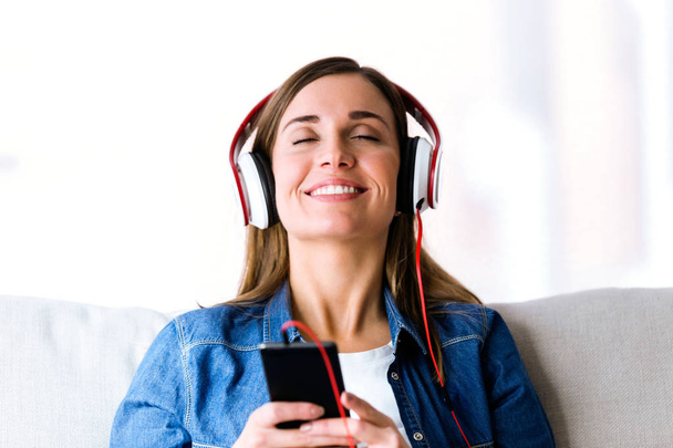 Beautiful young woman listening to music with mobile phone at home. - Foto, immagini