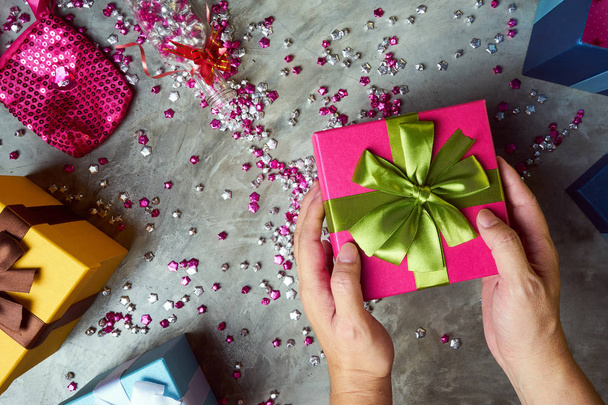 Close up of male hands holding gift with colorful box and little pink stars on grey background  - Photo, Image