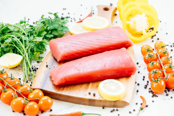 Rauwe tonijn filet visvlees op houten snijplank met groente- en ingrediënt voor het koken - Foto, afbeelding