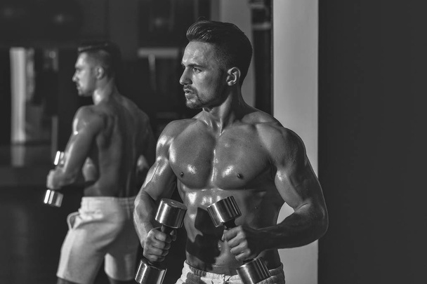 Handsome young man with sexy muscular wet body bare torso and chest training with heavy dumbbell in gym - Fotografie, Obrázek