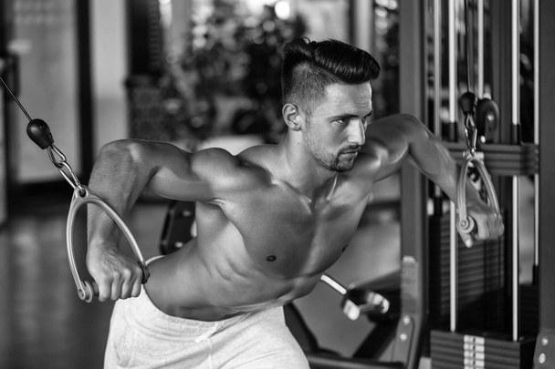 Handsome young man with sexy muscular wet body and bare back training with heavy exercise equipment in gym - Photo, image