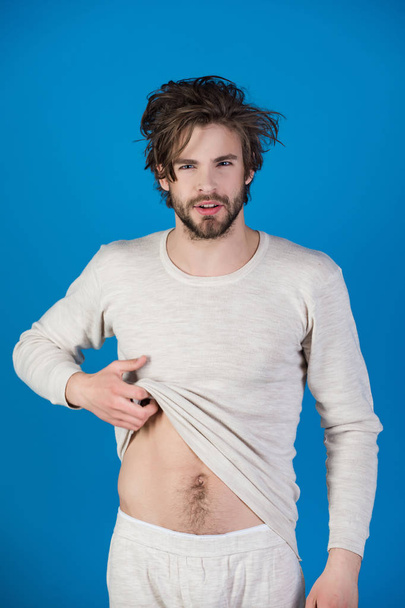 Morning wake up, everyday life. Insomnia, energy, single with uncombed hair. Barber and hairdresser, male fashion. Man with disheveled hair in underwear. Sleepy man with beard on blue background. - Fotografie, Obrázek