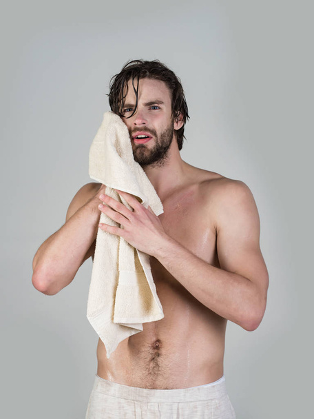 Man in bathroom with muscular body on grey background. Hygiene, sexy guy wash, spa, relax. Morning washing, wake up, everyday life. Refreshment, healthcare. Man with wet hair hold towel after shower. - Photo, image