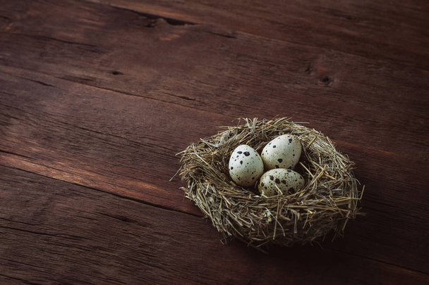Quail eggs in a nest on a wooden background. Taken at an angle - Zdjęcie, obraz