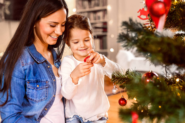 Young mother with daughter decorating Christmas tree together. - Φωτογραφία, εικόνα