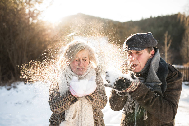 Beautiful senior couple blowing snow in sunny winter nature - Photo, image