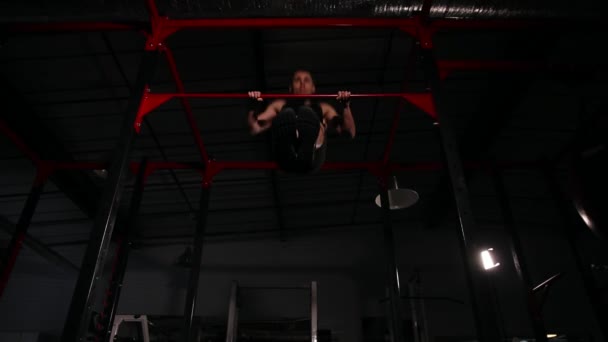 De atleet in zwarte kleding in de sportschool voert een stopcontact op de horizontale balk. Een brede hoekmening van onderen. - Video