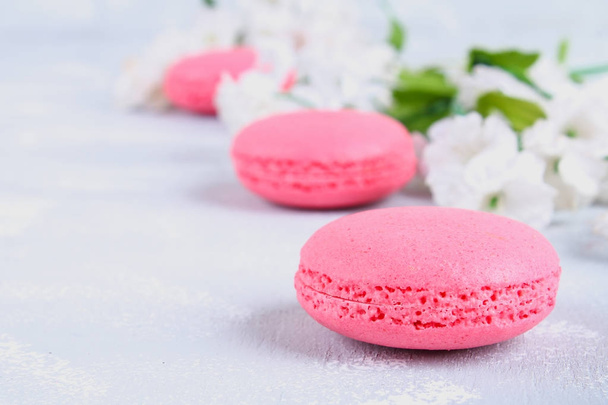 Pink and purple macaroons on a gray table surrounded by pink and white flowers. - Zdjęcie, obraz