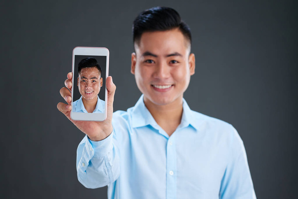 Onnellinen nuori aasialainen mies osoittaa älypuhelin hänen kasvonsa tunnistetaan
 - Valokuva, kuva