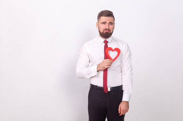 businessman crying and holding decorative heart while poising on gray background, concept of broken heart on valentines day  - Fotoğraf, Görsel