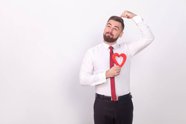 thoughtful businessman holding decorative heart and poising on gray background, valentines day concept - 写真・画像