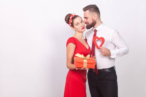 romantic couple hugging while holding gift box and decorative heart on gray background, valentines day concept - Fotó, kép