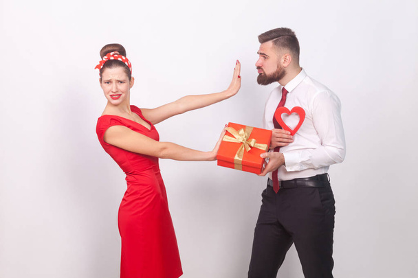 Woman in red dress ignoring and refusing businessman with gift and heart in hands on gray background, valentines day concept - Photo, Image