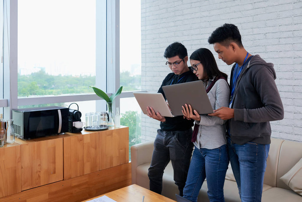Csoport-ázsiai fejlesztők tartja laptopok hivatalban és látszó-on idegen rádióadást figyel képernyő - Fotó, kép
