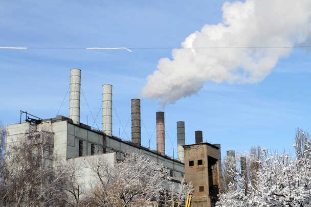 Зимний промышленный ландшафт с заводами и большим количеством дымящихся труб. Снежная зима в промышленном городе
. - Фото, изображение
