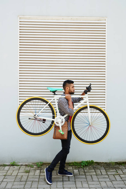 Young Indian man carrying his bicycle in the street - Foto, imagen