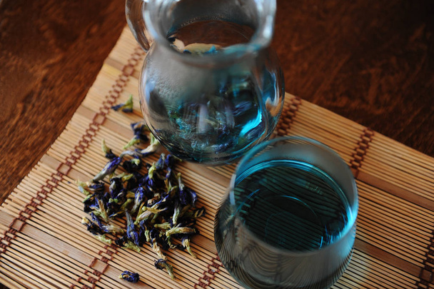 Caraffa e bicchiere con tè blu Thai Anchan su tappetino di bambù su tavolo di legno. Posizionatore di fiori per la produzione di birra, vista dall'alto
 - Foto, immagini