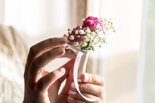 Невеста держит пуговицу. Нежная рука невесты, держащей бутоньерку для жениха - Фото, изображение