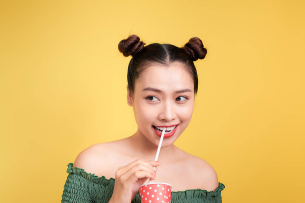 Beautiful young smiling asian girl with red lips drinking cola with straw  - Zdjęcie, obraz